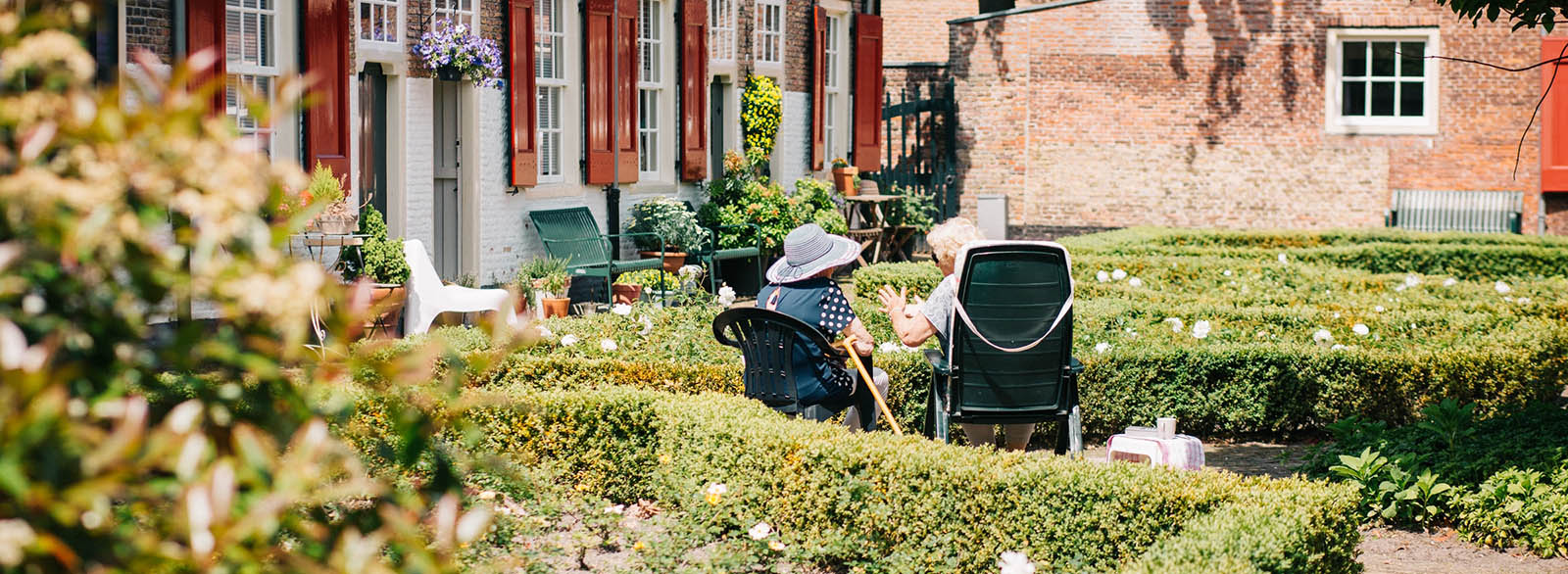 Two elderly individuals having a discussion in a garden setting.