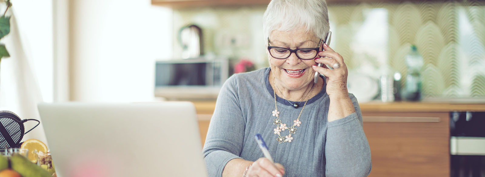 Older woman on cell phone in front of laptop.