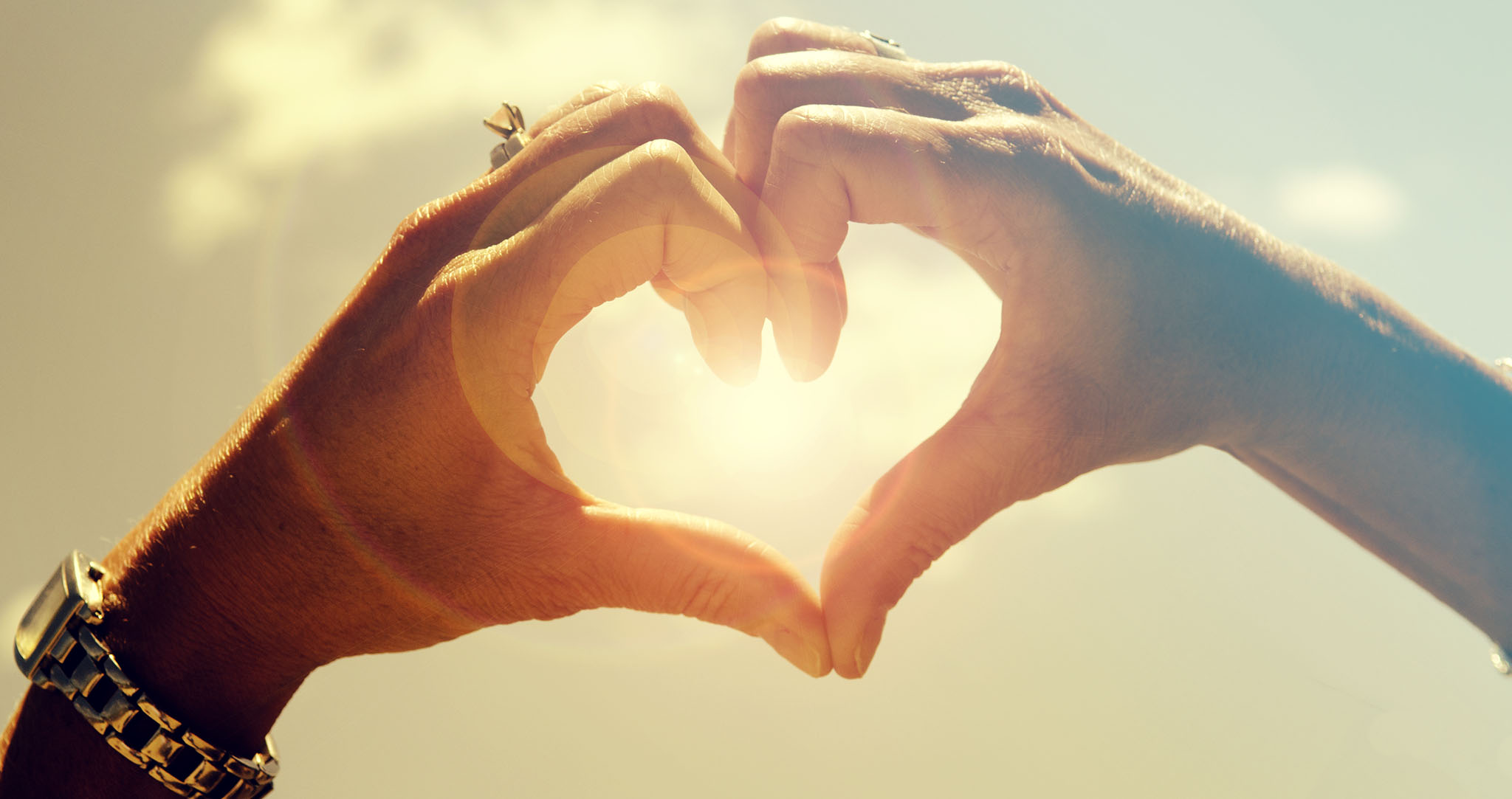 Hands forming a heart with sun in background